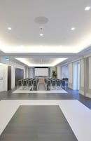 Una sala conferenze con file di sedie, uno schermo per proiettore e una lavagna di grandi dimensioni.