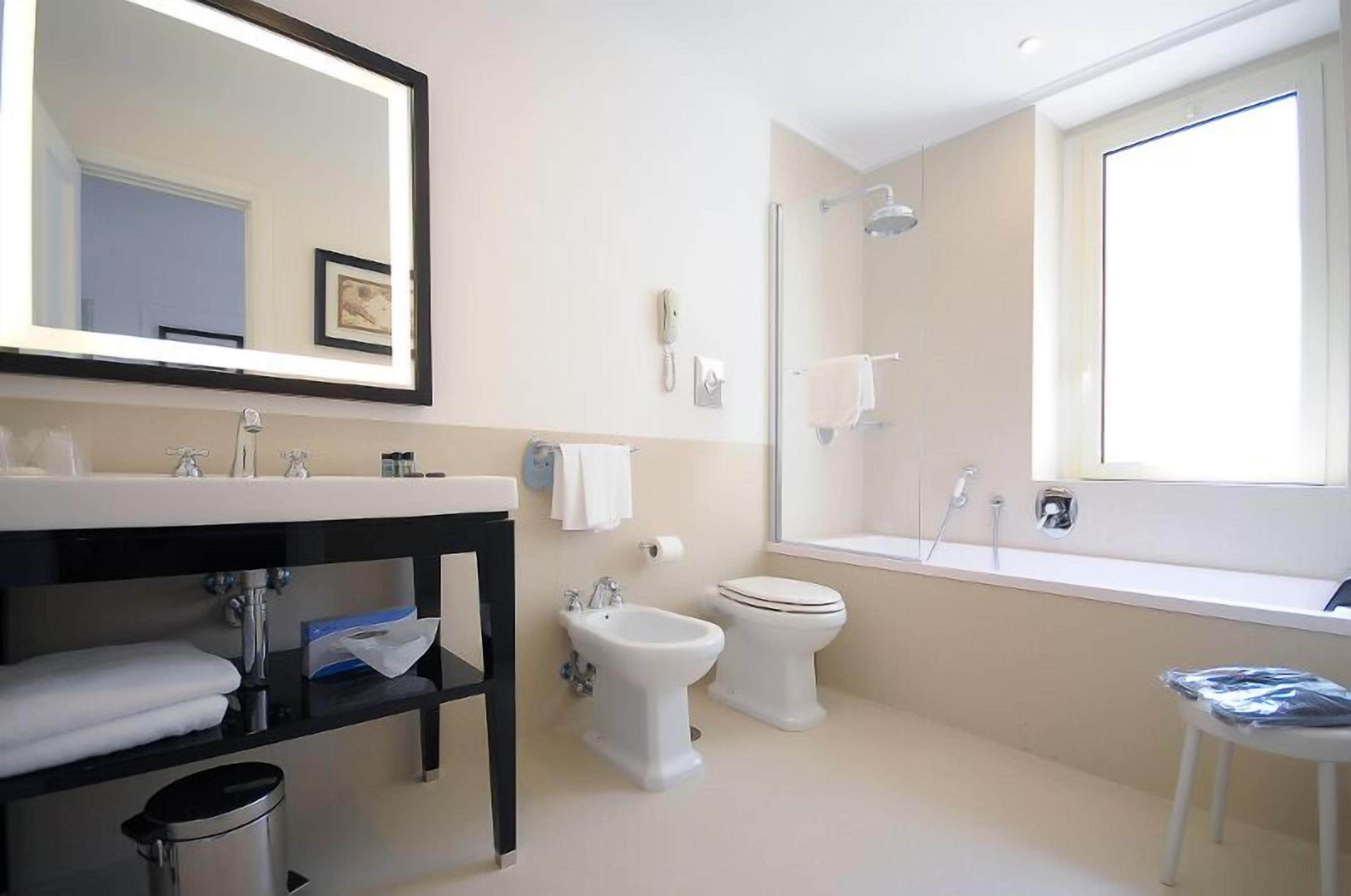 A modern bathroom with a large mirror, a bidet, a toilet, and a shower.
