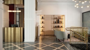 Un vestíbulo de hotel con mostrador de recepción, zona de estar, una escalera y una estantería decorativa con jarrones.