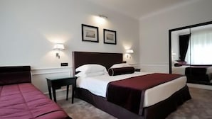 Una habitación de hotel con una cama grande, dos mesitas de noche, un escritorio y un espejo.