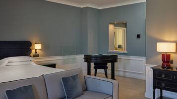 A hotel room with a bed, a piano, a sofa, a nightstand, and a mirror.