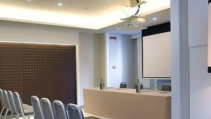 Une salle de conférence moderne équipée d’une longue table, de plusieurs chaises, d’un pupitre et d’un grand écran.