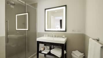 A modern bathroom with a glass-enclosed shower, a white sink with a mirror above it, and a small stool with a towel.
