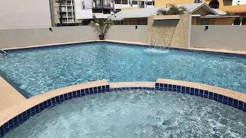 Une piscine à l’eau d’un bleu limpide, entourée d’une terrasse carrelée et d’un petit muret.