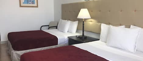 Habitación de hotel con dos camas, cabecero, mesita de noche, lámpara, una silla y un cuadro enmarcado en la pared.