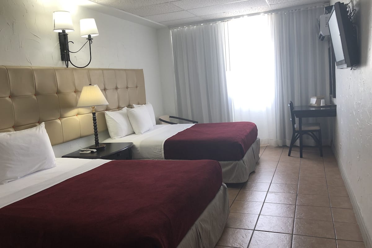 Habitación de hotel con dos camas, un escritorio, una silla, un televisor y una ventana con cortinas.