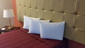 Habitación de hotel con cabecera capitonada, dos almohadas blancas, una colcha roja y una lámpara de mesa en la mesita de noche.