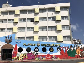 Un edificio con varias unidades de aire acondicionado, un mural con el nombre 'Platos Restaurant' y 'Cocina Puertorriqueña & Bar', y un logo de Coca-Cola.