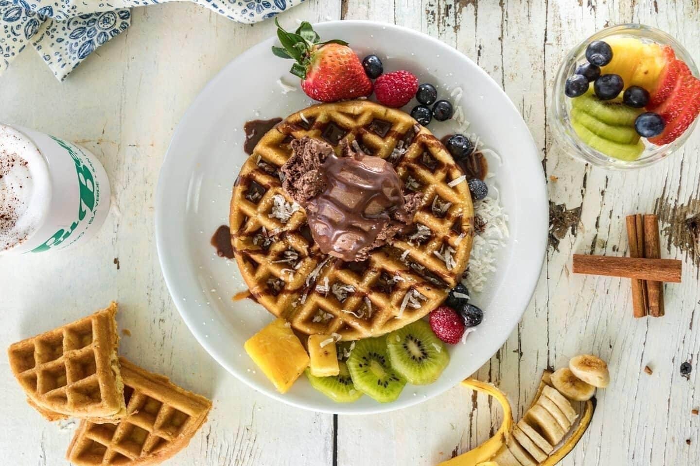 A plate of waffles with chocolate sauce, strawberries, blueberries, kiwi, and banana slices.