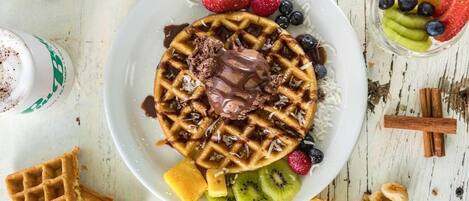A plate of waffles with chocolate sauce, strawberries, blueberries, kiwi, and banana slices.