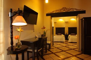 A hotel room with a dining area, a TV mounted on the wall, a bed with a white bedspread, and a tiled floor.