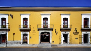 Un bâtiment jaune doté de trois balcons, chacun orné d’une balustrade en fer forgé et de plantes en pot.