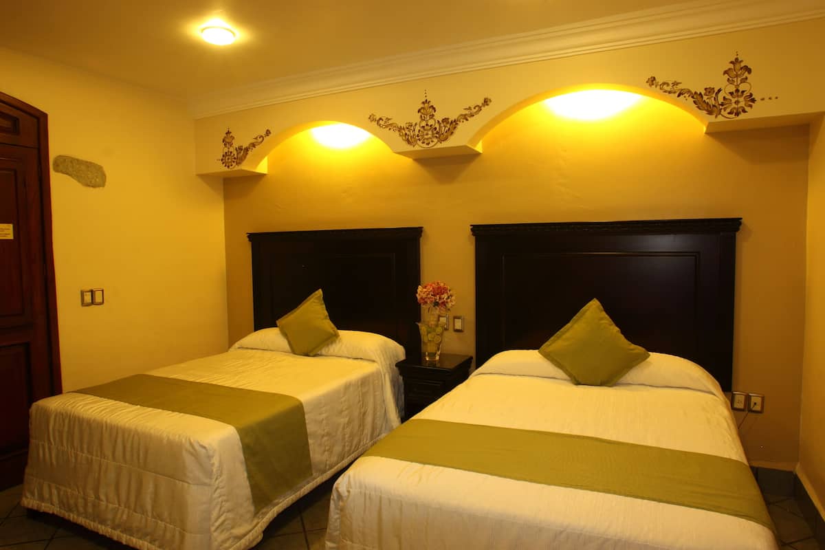 Habitación de hotel con dos camas individuales, cada una con cubrecama y almohadas verdes a juego. Entre las camas, una mesita de noche con un jarrón de flores.