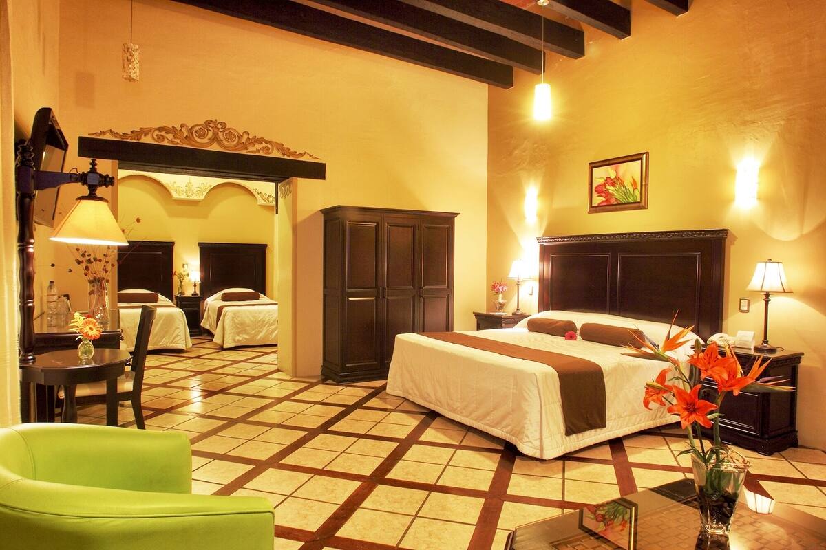 Una habitación de hotel con una cama, dos mesitas de noche, una silla, un armario y un espejo.