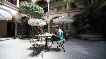 Un patio al aire libre con mesas y sillas, rodeado de plantas y una fuente.