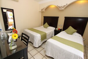 Una habitación de hotel con dos camas individuales, un escritorio con un florero y un espejo en la pared.
