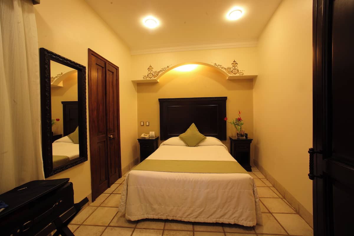 Una habitación de hotel con una cama, una mesita de noche, un espejo y una puerta.