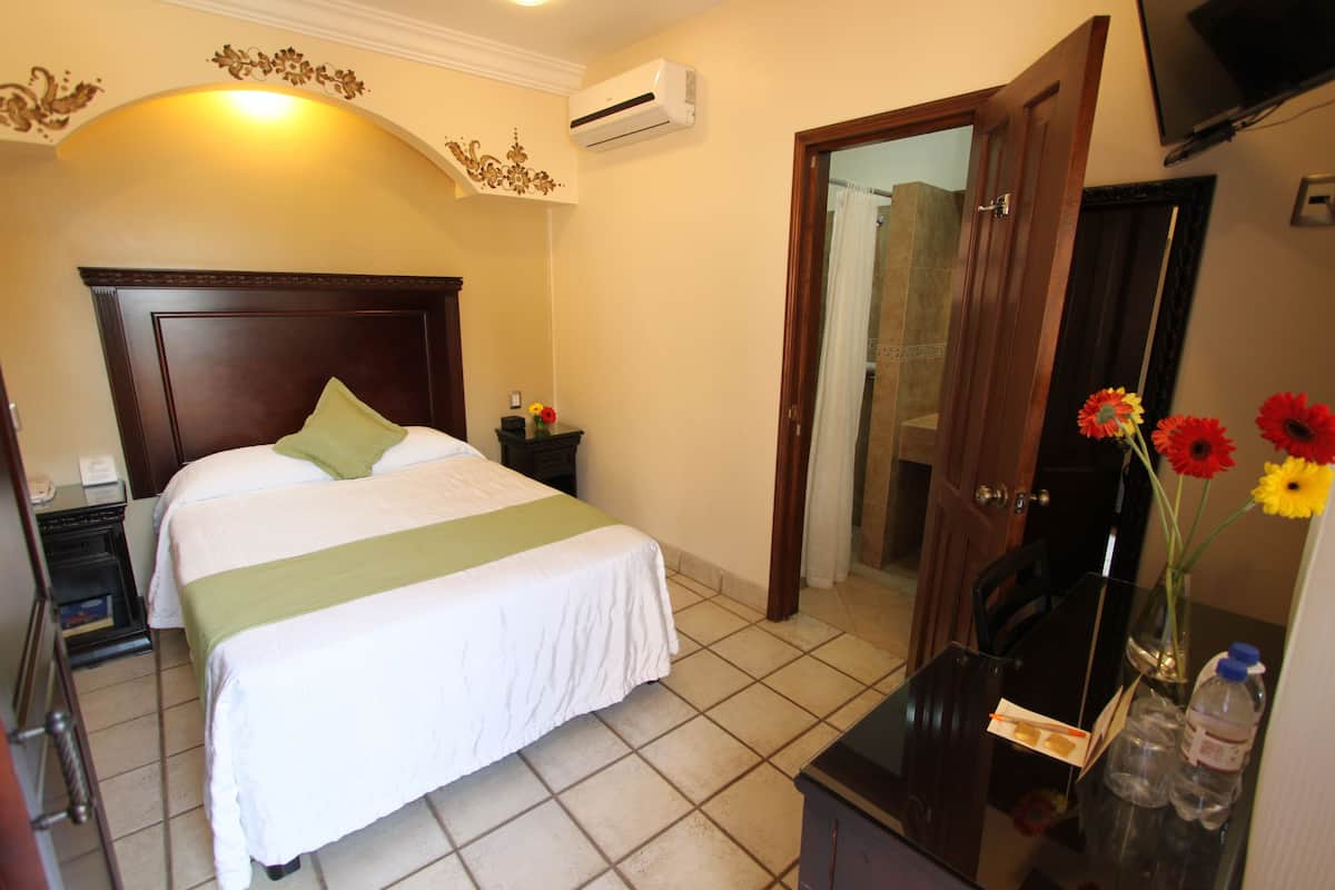 Una habitación de hotel con una cama, mesita de noche y un espejo.