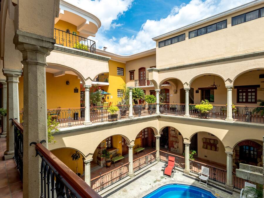 Un patio de varios niveles con zonas de estar al aire libre, una piscina y una mezcla de estilos arquitectónicos que incluyen arcos y columnas.