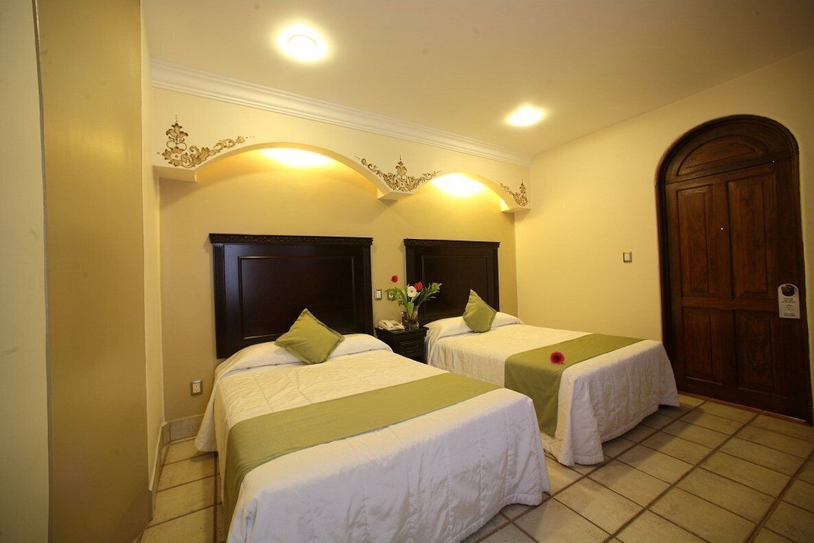 Habitación de hotel con dos camas individuales, una puerta de madera y una mesita con un florero.