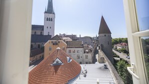 Une vue depuis une fenêtre donnant sur une rue bordée d’immeubles, dont une église dotée d’un flèche haute et une construction qui ressemble à un château.