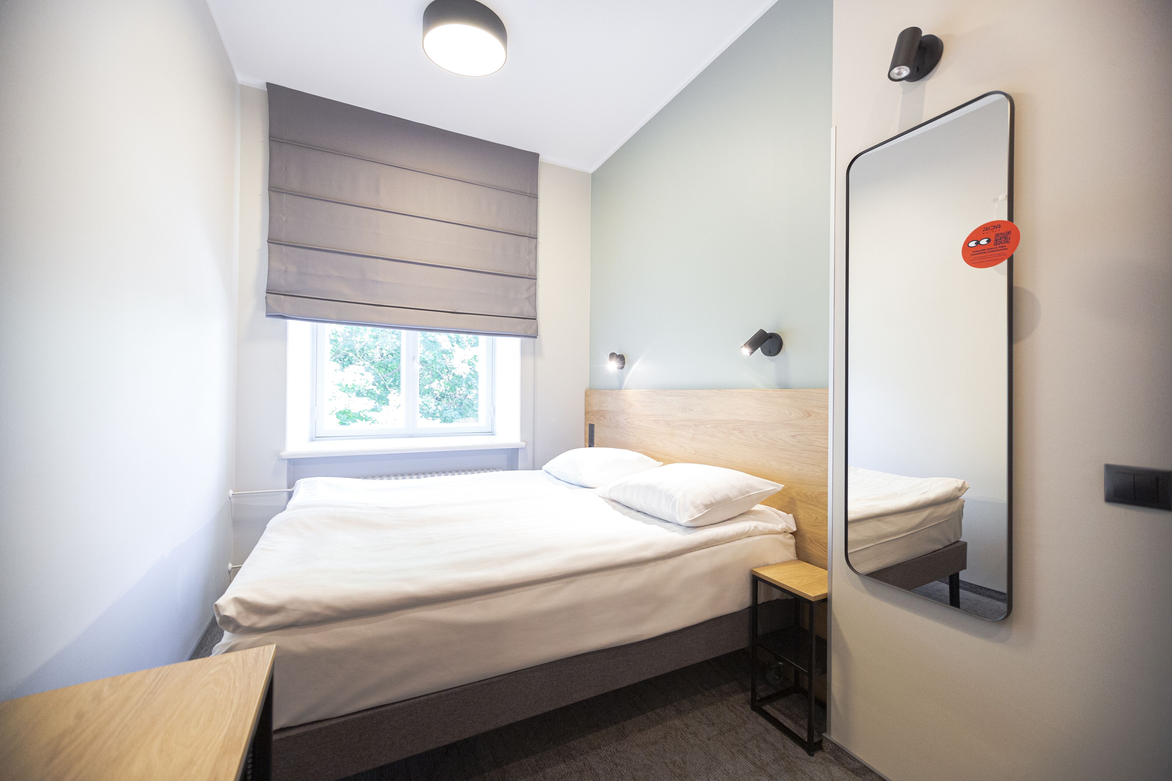A modern bedroom with a bed, bedside table, and a large mirror.