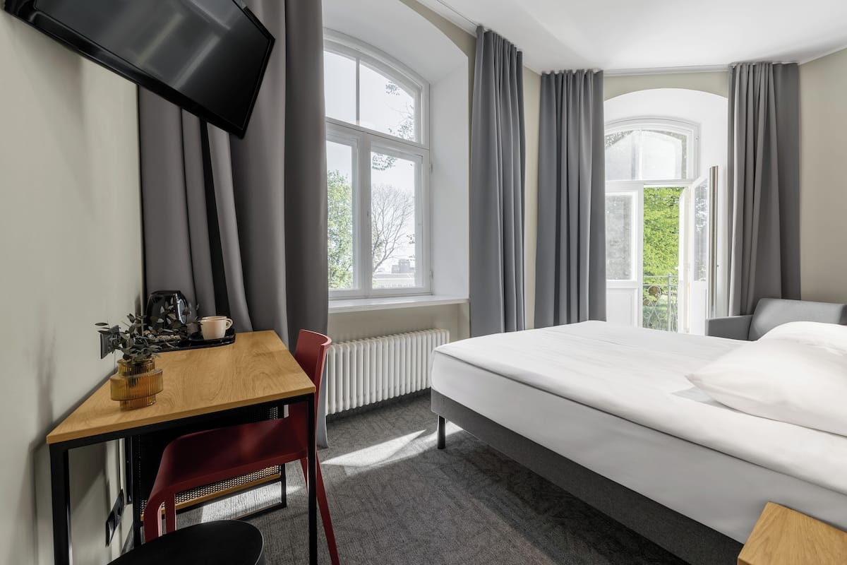 Ein Hotelzimmer mit Bett, Schreibtisch, Stuhl, Fernseher und einem Fenster mit Vorhängen.