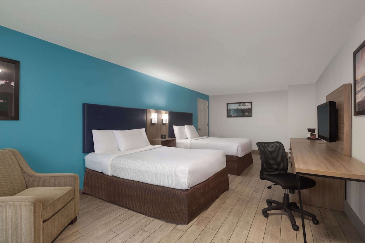 Ein Hotelzimmer mit zwei Betten, einem Schreibtisch, einem Stuhl und einem Fernseher.