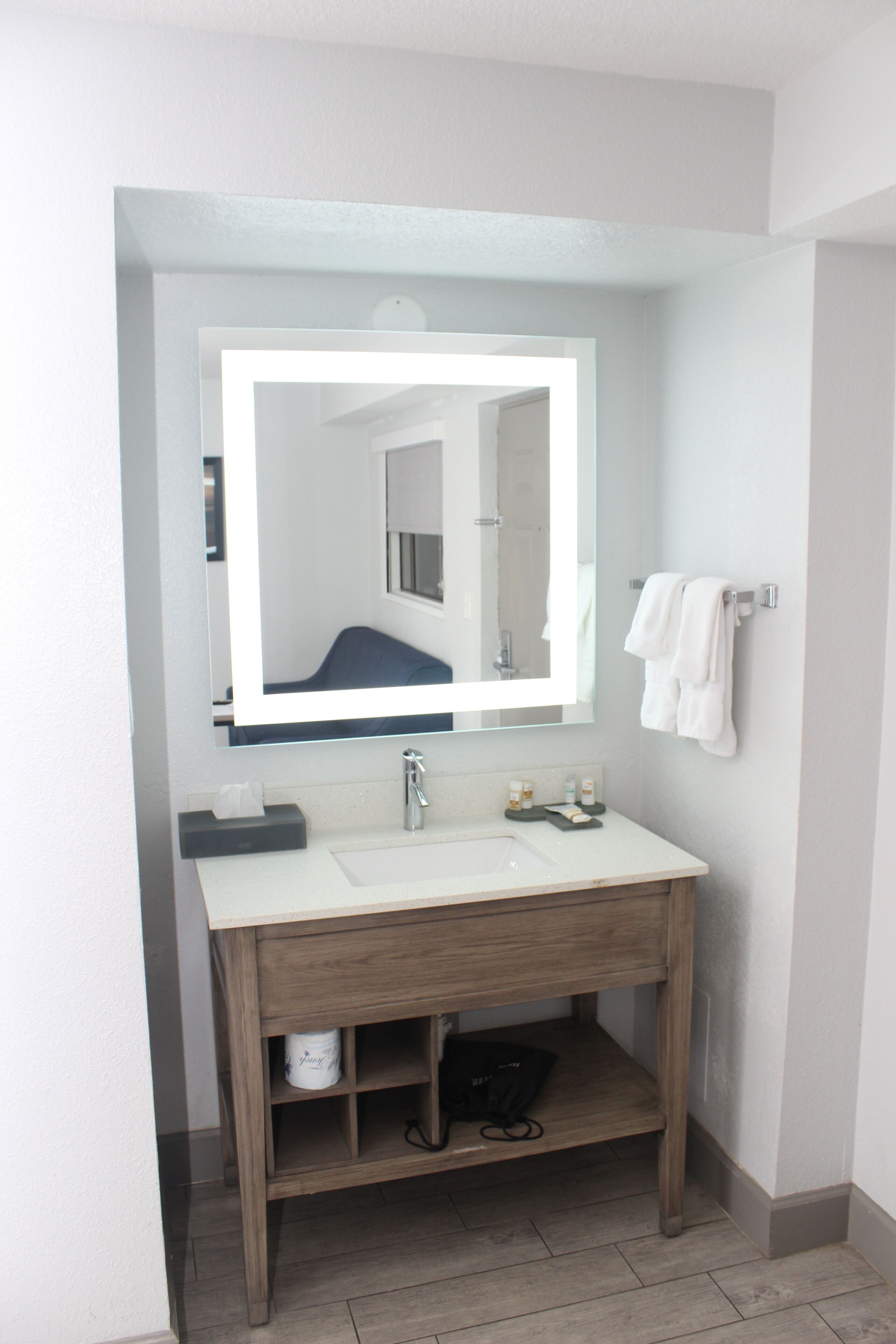 A bathroom with a white sink, a mirror, a towel rack, and a wooden vanity.