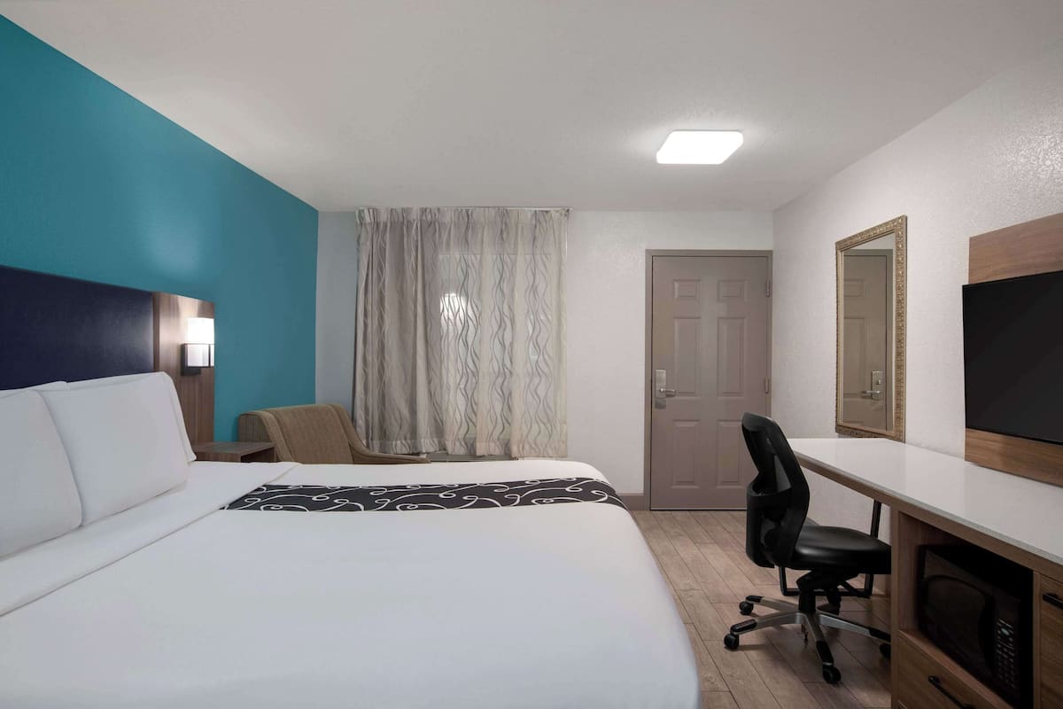 Ein Hotelzimmer mit einem großen Bett, einem Schreibtisch mit Stuhl, einem Fernseher und einer Tür.