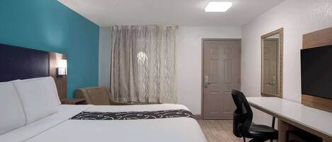 A hotel room with a large bed, a desk with a chair, a TV, and a door.
