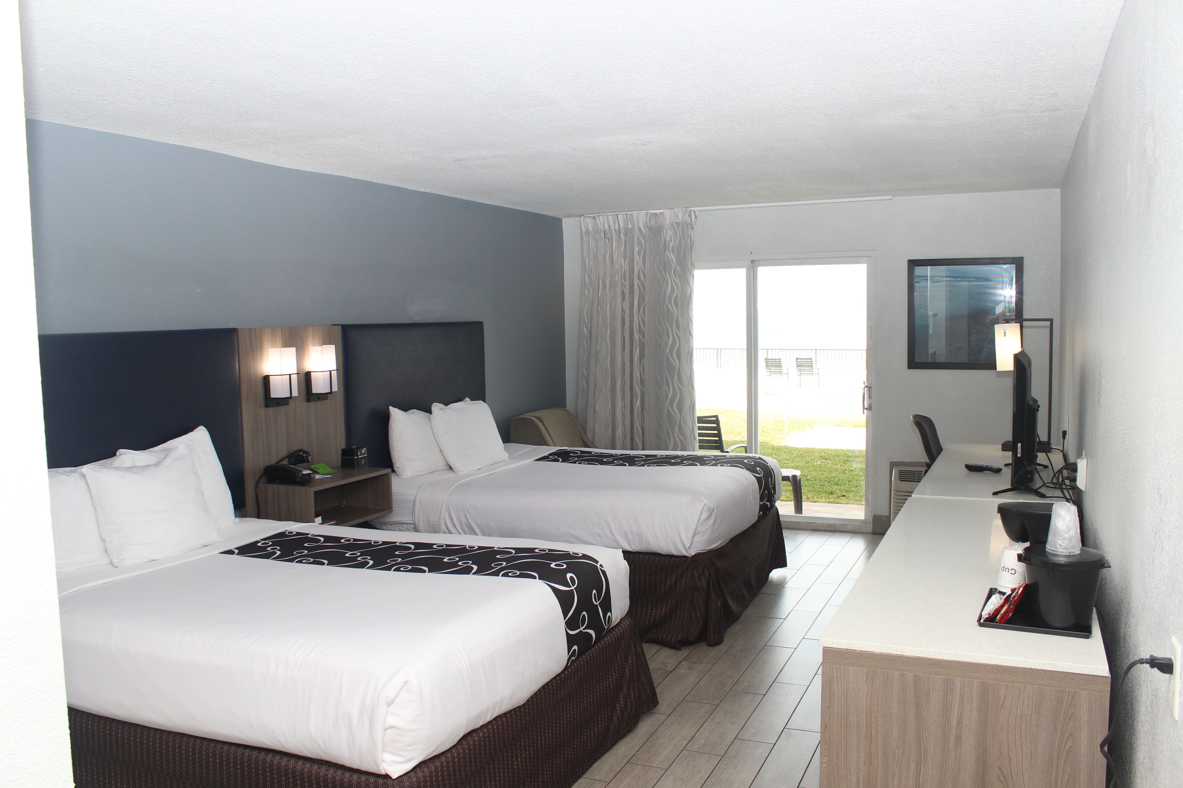 Een hotelkamer met twee bedden, een bureau, een stoel, een lamp en een raam met gordijnen.