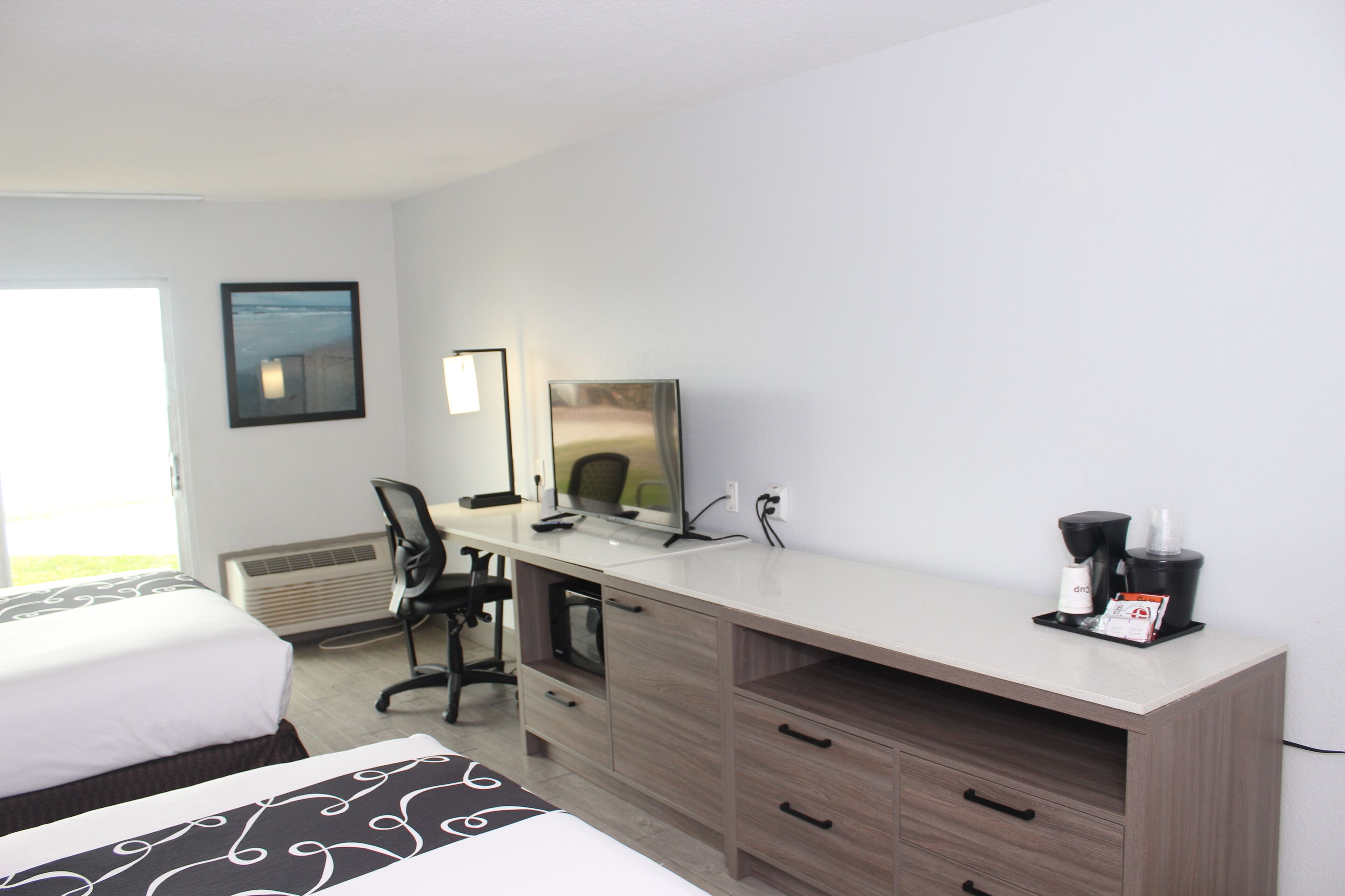 A hotel room with a bed, a desk with a computer, a chair, a coffee maker, and a window with a view.