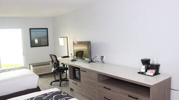 A hotel room with a bed, a desk with a computer, a chair, a coffee maker, and a window with a view.