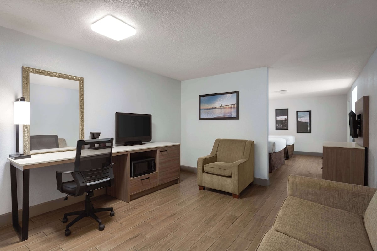 Ein modernes Hotelzimmer mit Schreibtisch, Bürostuhl, Fernseher und einer Couch.