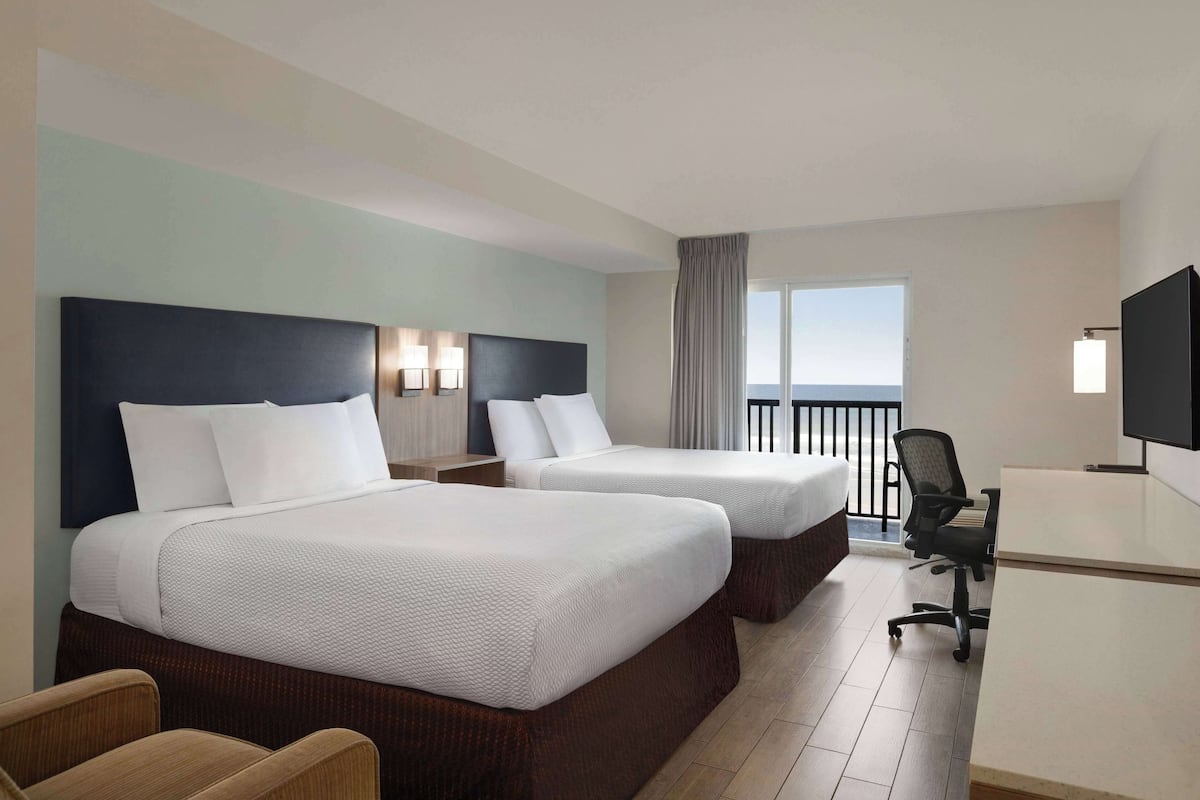 Ein Hotelzimmer mit zwei Betten, einem Schreibtisch, einem Stuhl und einem Fernseher.