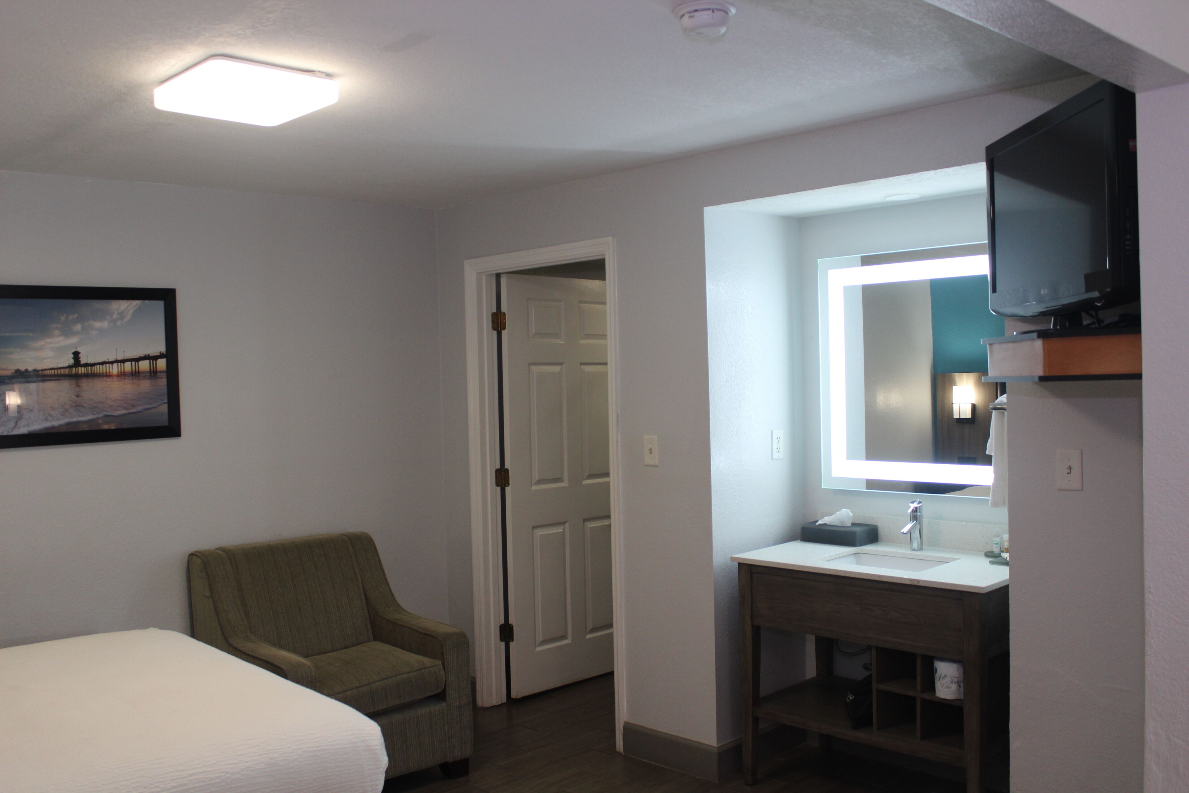 A hotel room with a bed, a chair, a bathroom with a sink and mirror, and a television.