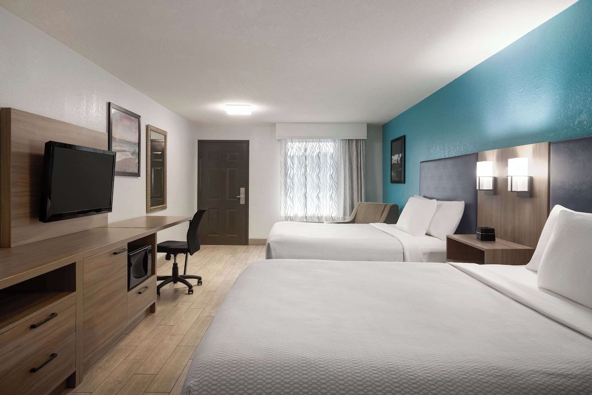 Ein Hotelzimmer mit zwei Betten, einem Schreibtisch mit Stuhl, einem Fernseher und einem Fenster mit Vorhängen.