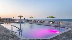Una piscina con vistas al mar, rodeada de sillones de playa y sombrillas.