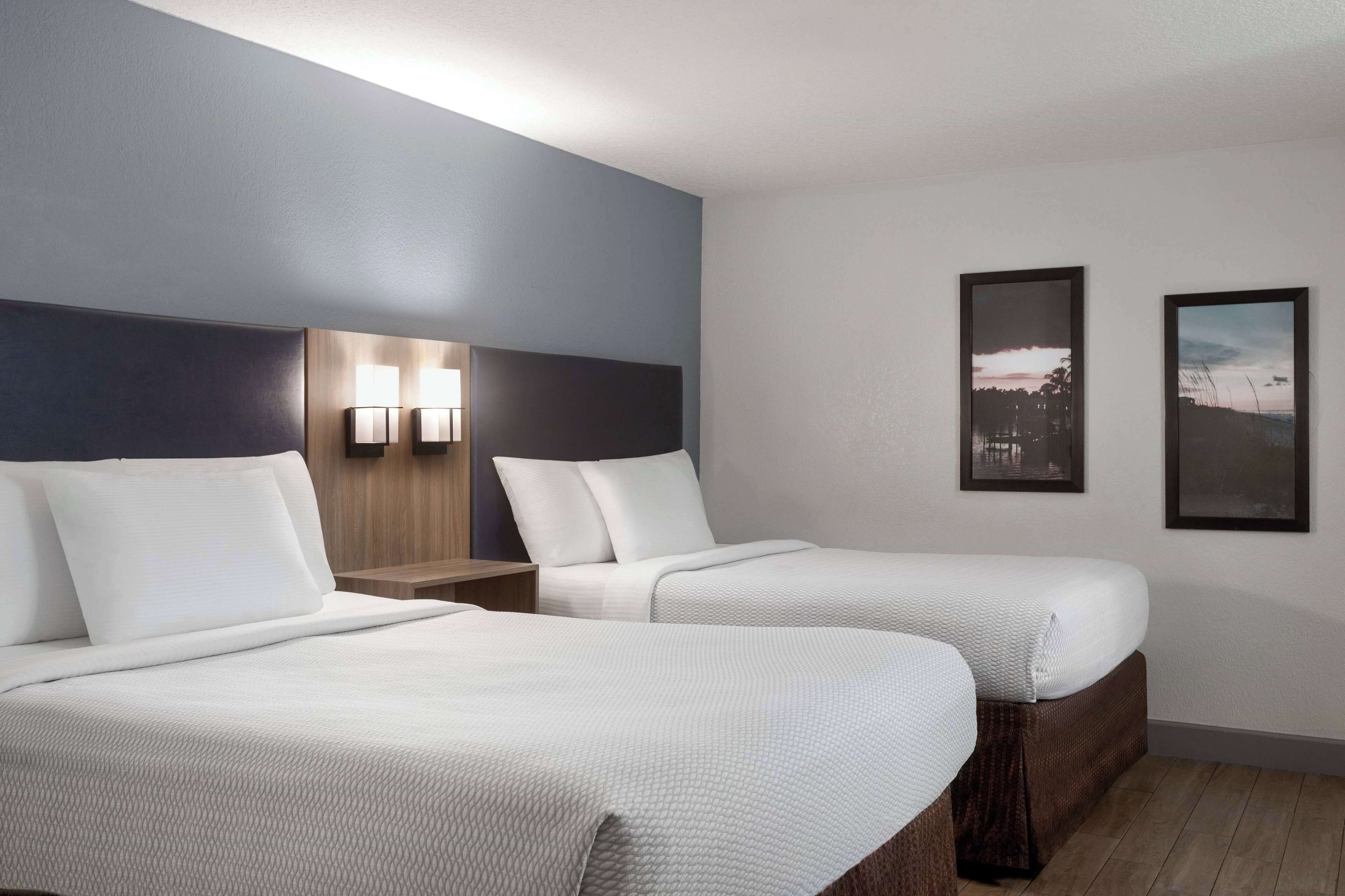 A hotel room with two beds, a nightstand with lamps, and two framed pictures on the wall.