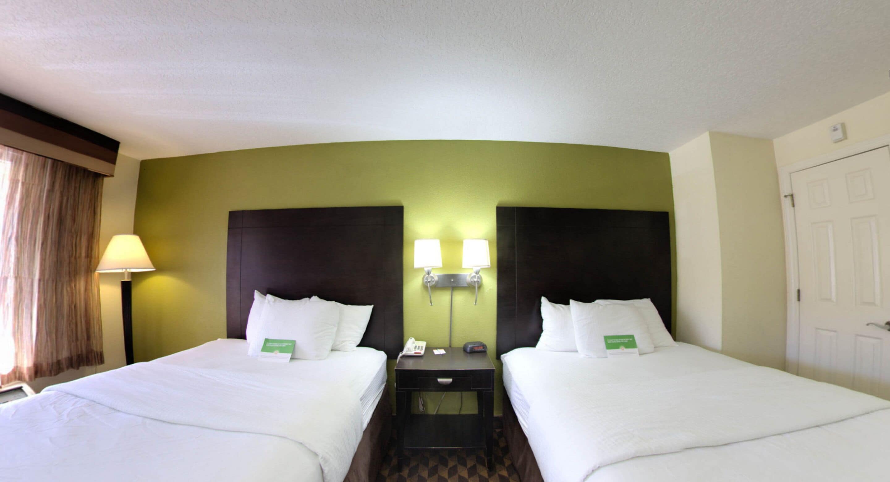 Habitación de hotel con dos camas, una mesita de noche con lámpara, teléfono y puerta.