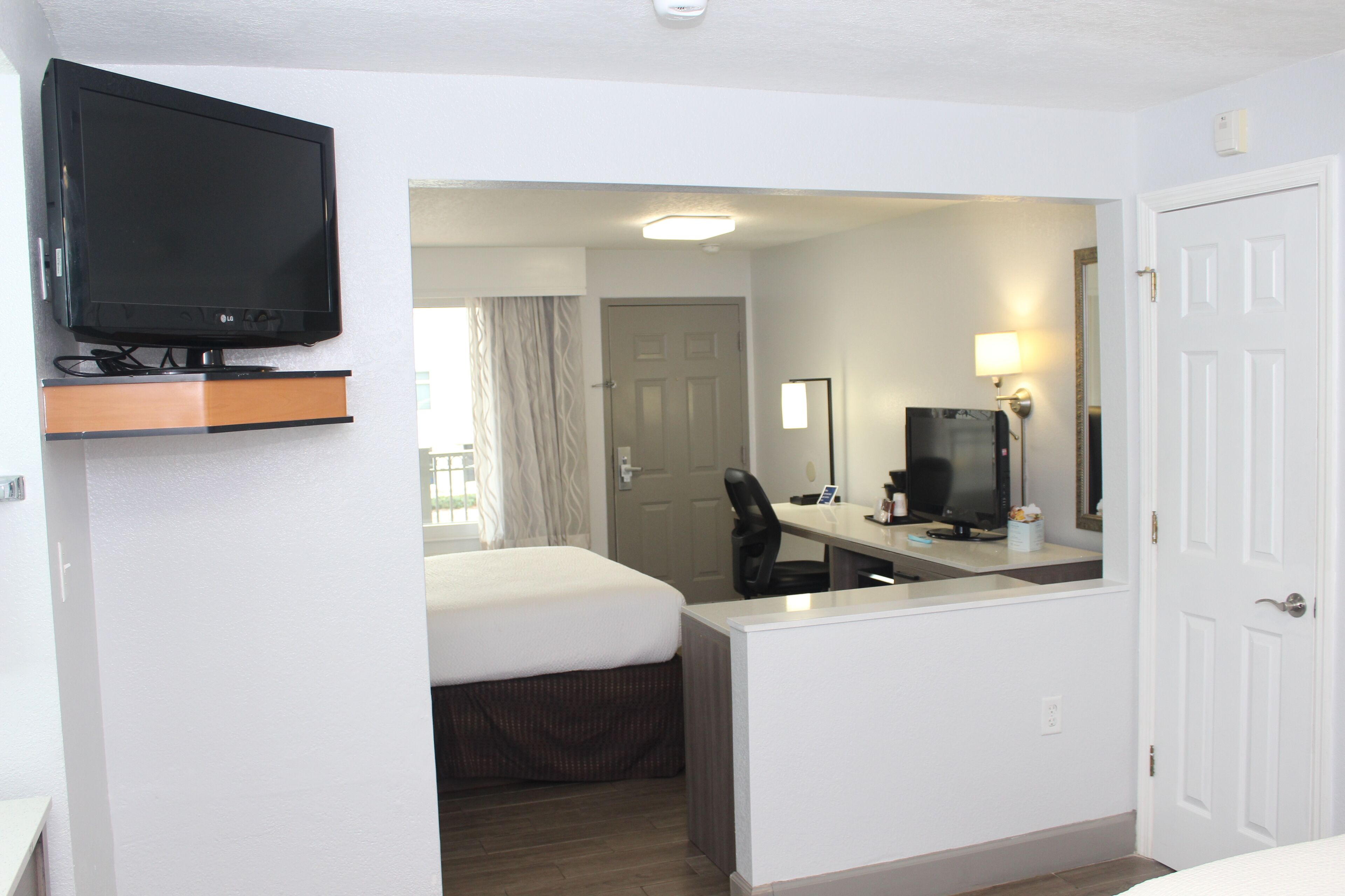 A hotel room with a bed, a desk with a computer, a TV, and a door.