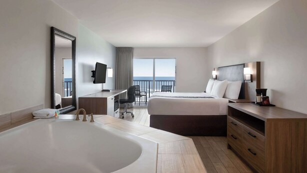 Habitación de hotel con una bañera grande, una cama con dos almohadas, un escritorio con una silla, un televisor y un balcón con vistas.