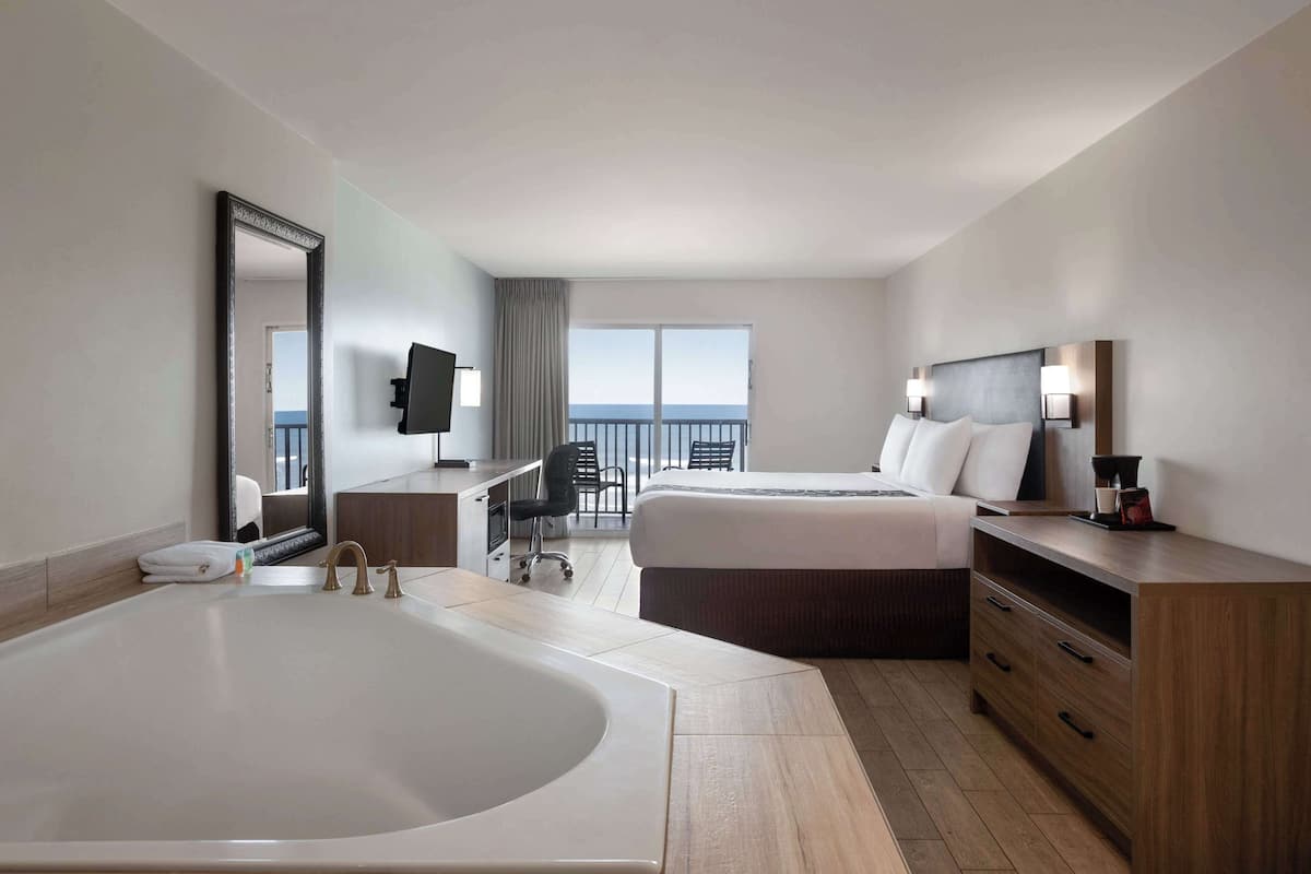 Ein Hotelzimmer mit einer Eckbadewanne, einem Bett mit zwei Kissen, einem Schreibtisch mit Stuhl, einem Fernseher und einem Balkon mit Blick.