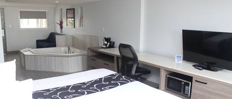Une chambre d’hôtel équipée d’un lit, d’un bureau, d’une chaise, d’une télévision, d’un four à micro-ondes et d’une baignoire.
