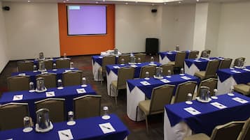 Un salón de conferencias con varias mesas, sillas y una pantalla de proyección.