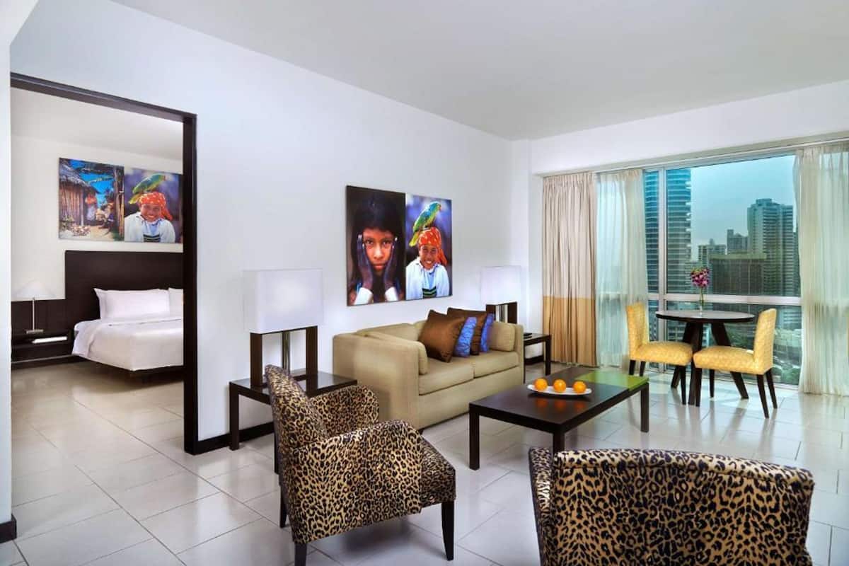 A hotel room with a bed, a sofa, two armchairs, a coffee table, and artwork on the walls.