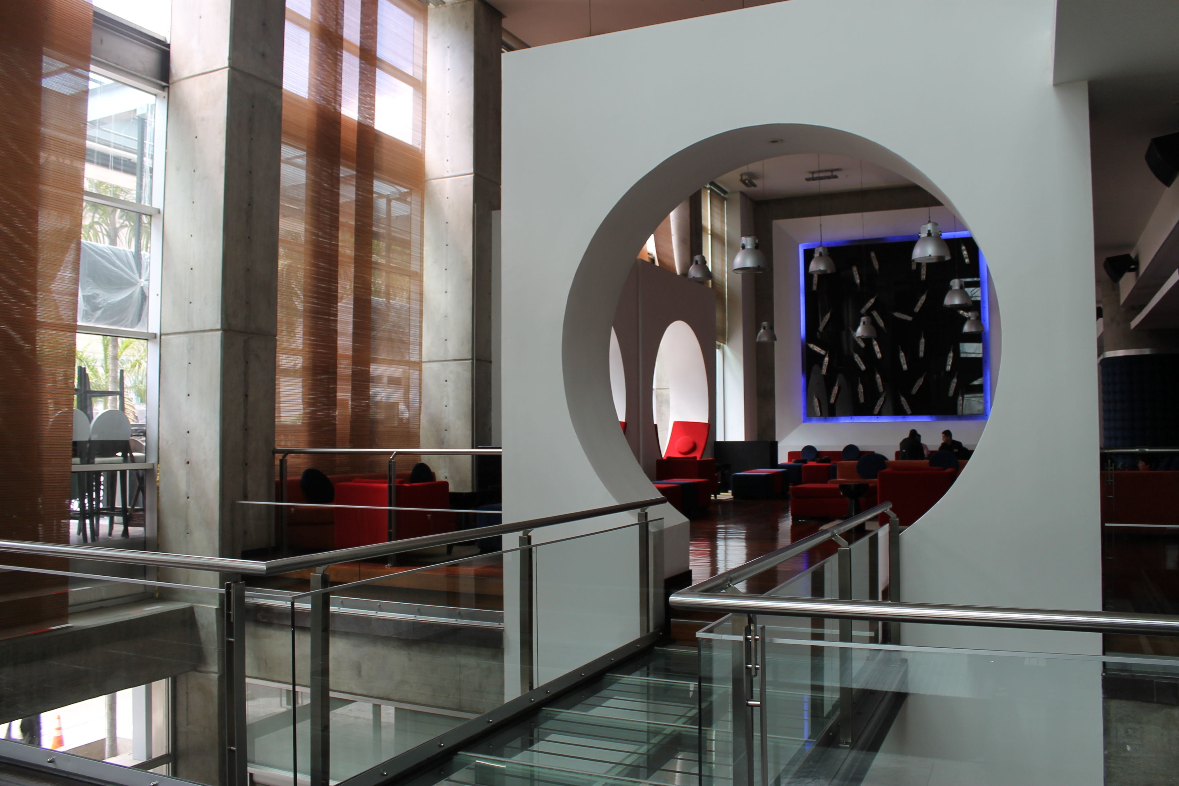 A modern interior with a glass staircase, red seating areas, and a central circular feature with artwork.