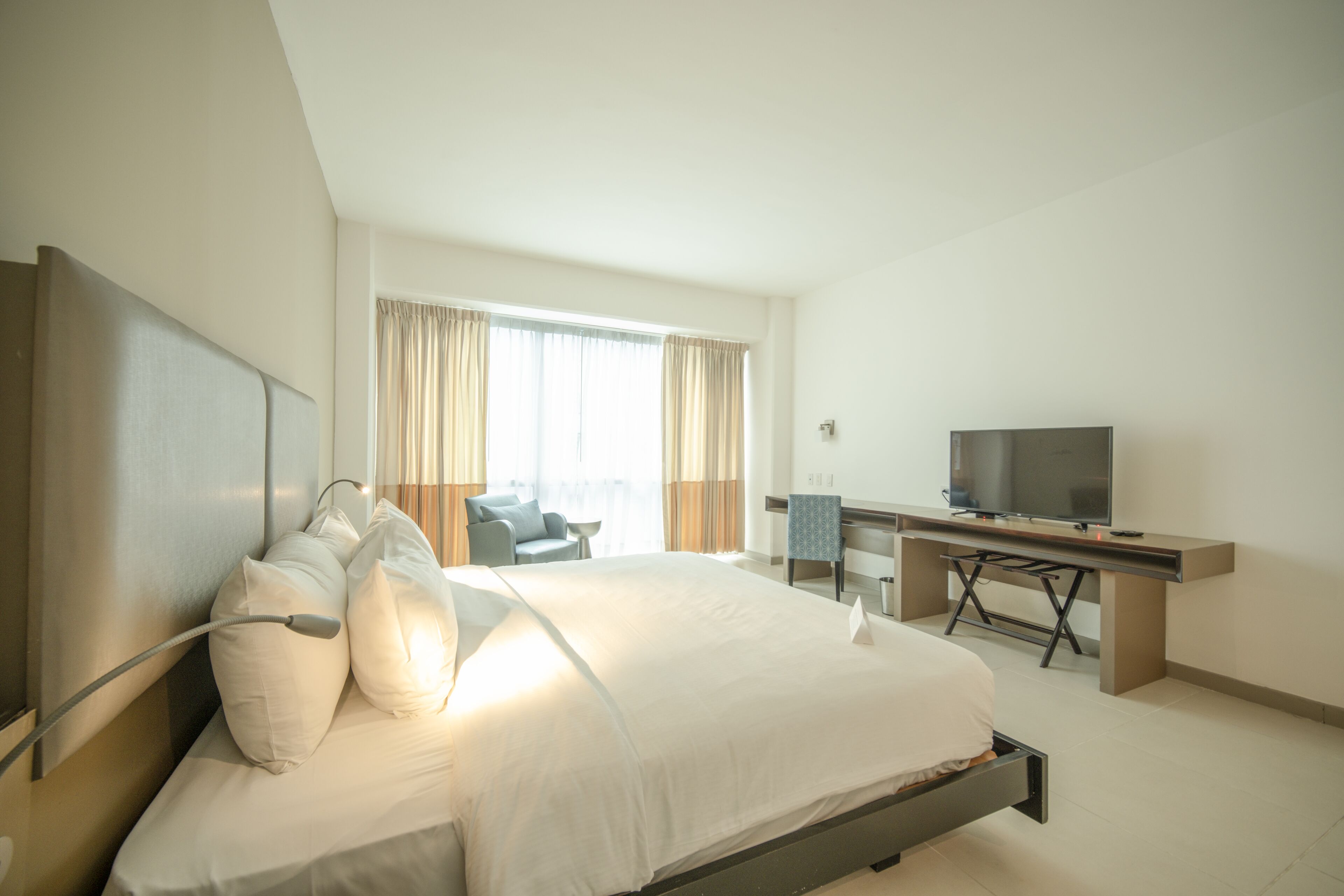 Habitación de hotel moderna con una cama grande, un escritorio, un televisor y vistas al exterior por la ventana.