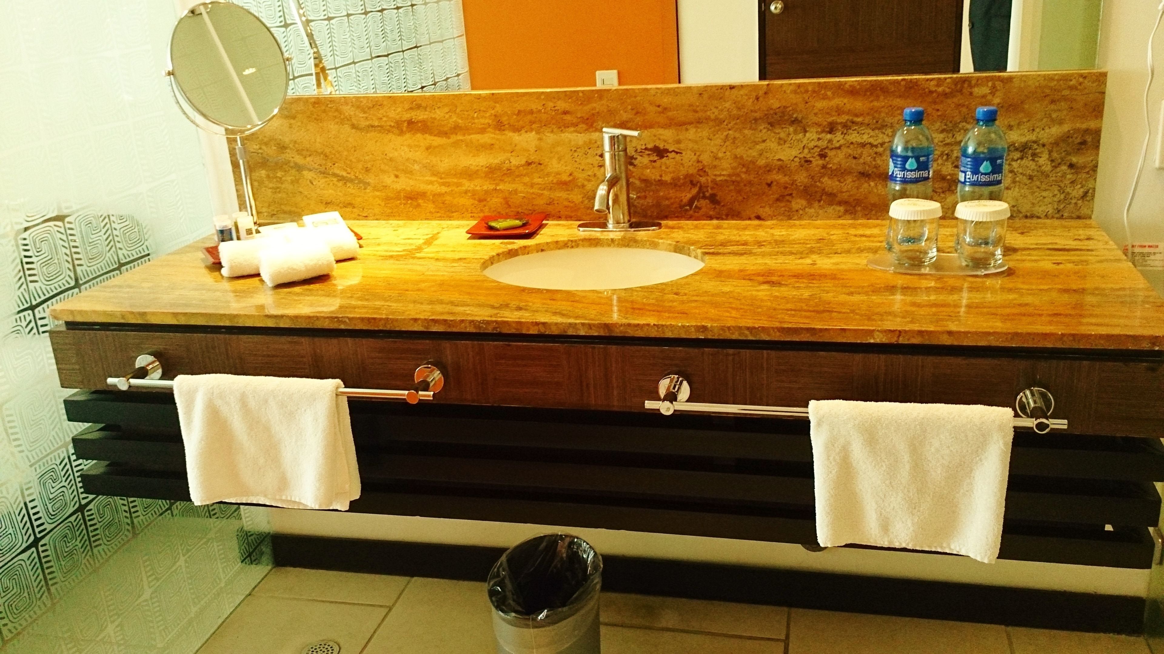Un baño con lavamanos de mármol, dos toalleros, un espejo y dos botellas de agua.